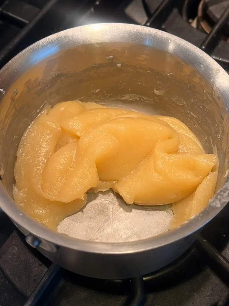 A thick, pale-gold reduction of sugar, flour, and cream in a metal saucepan, cooked down until it pulls away from the sides.