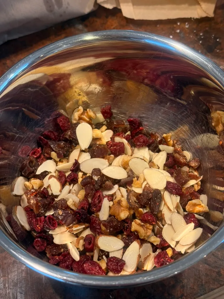 A metal bowl of sliced almonds, crushed walnuts, dried cranberries, and chopped dates ready to fold in.