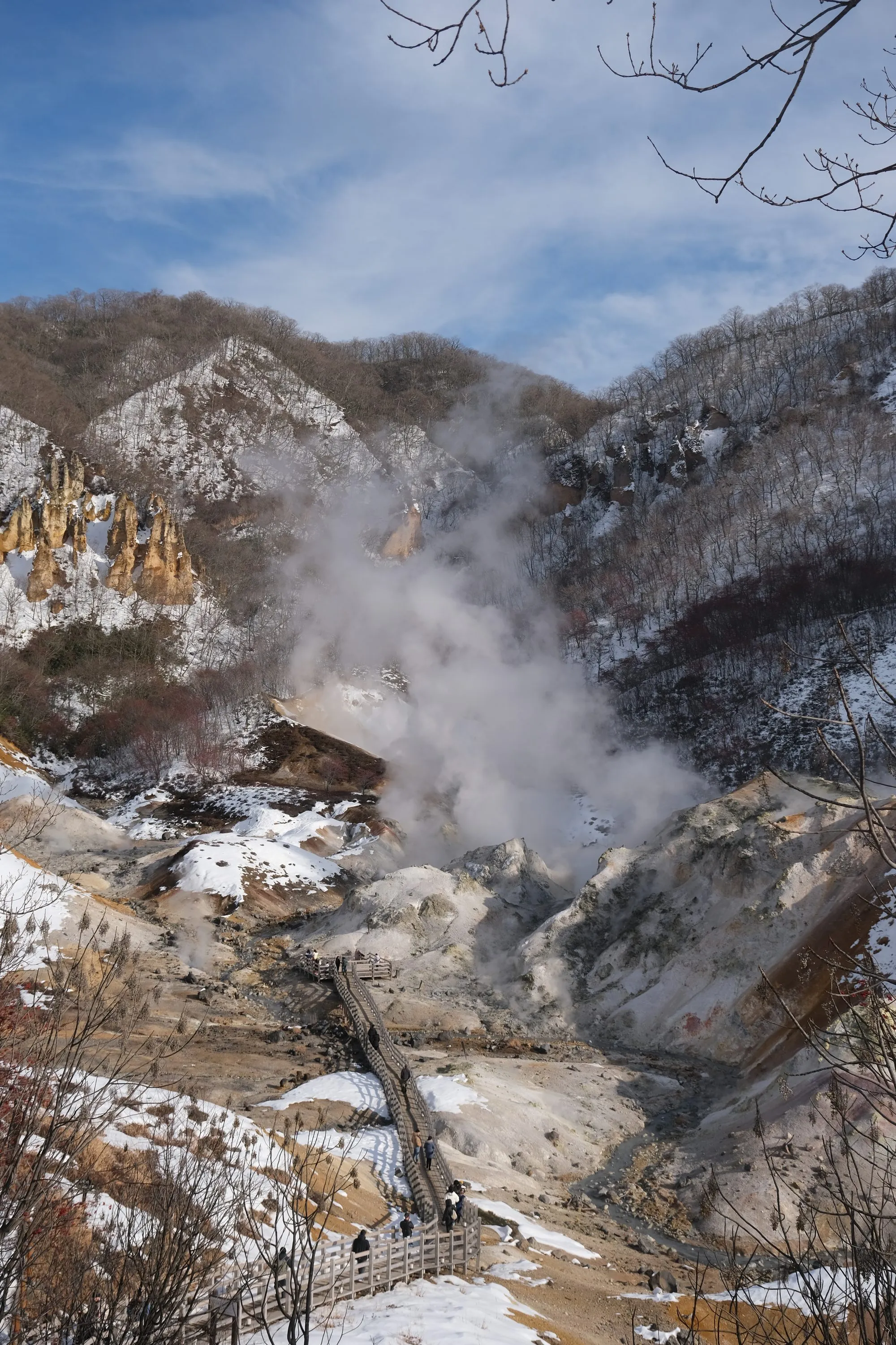 Steam rising from the geothermal hell valley above Noboribetsu, with a boardwalk winding through the snowy, mineral-streaked slopes.