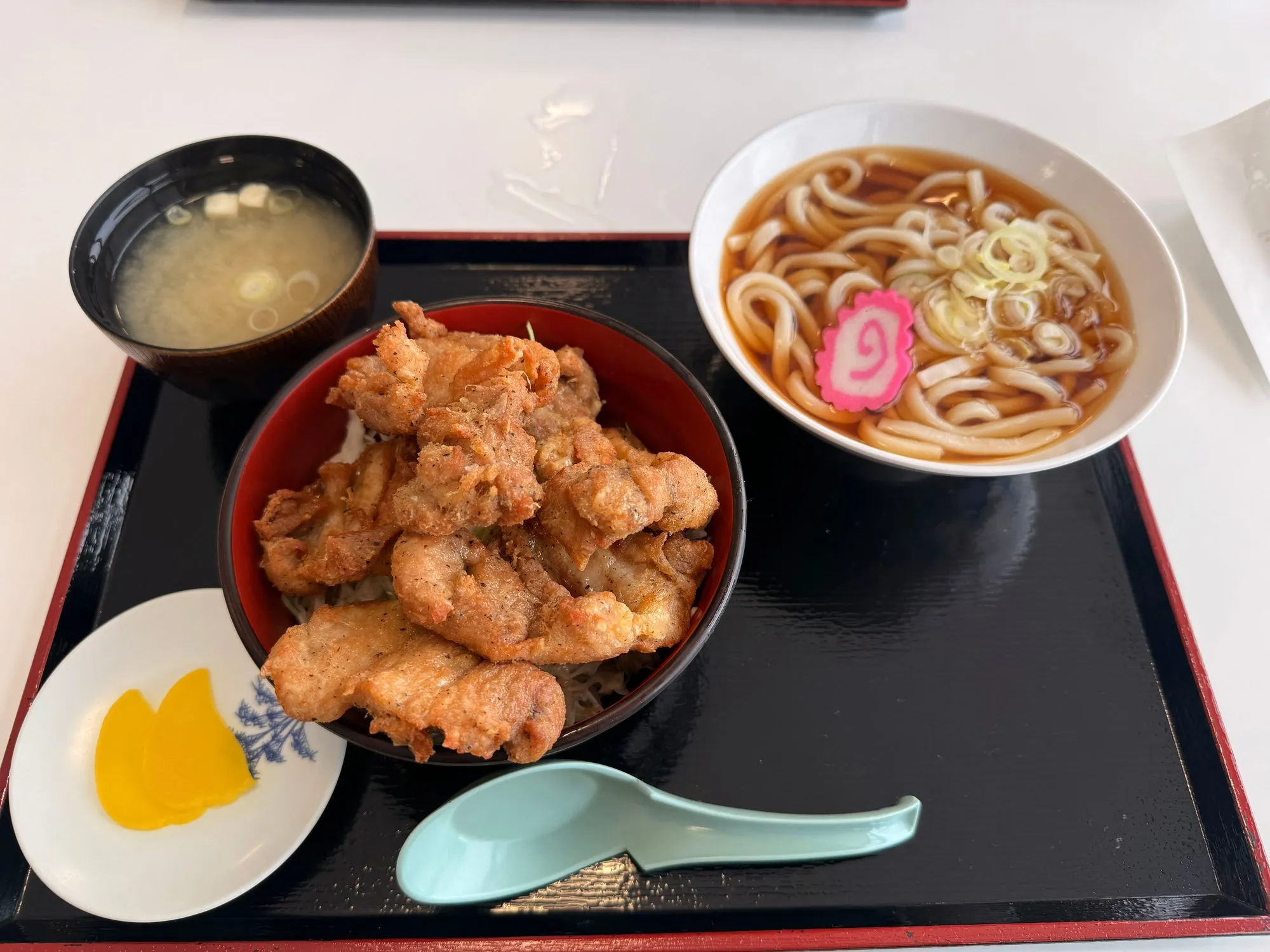 A lunch tray at the Pippu lodge: a bowl of karaage over rice, a bowl of udon in broth with fish cake, miso soup, and pickles.