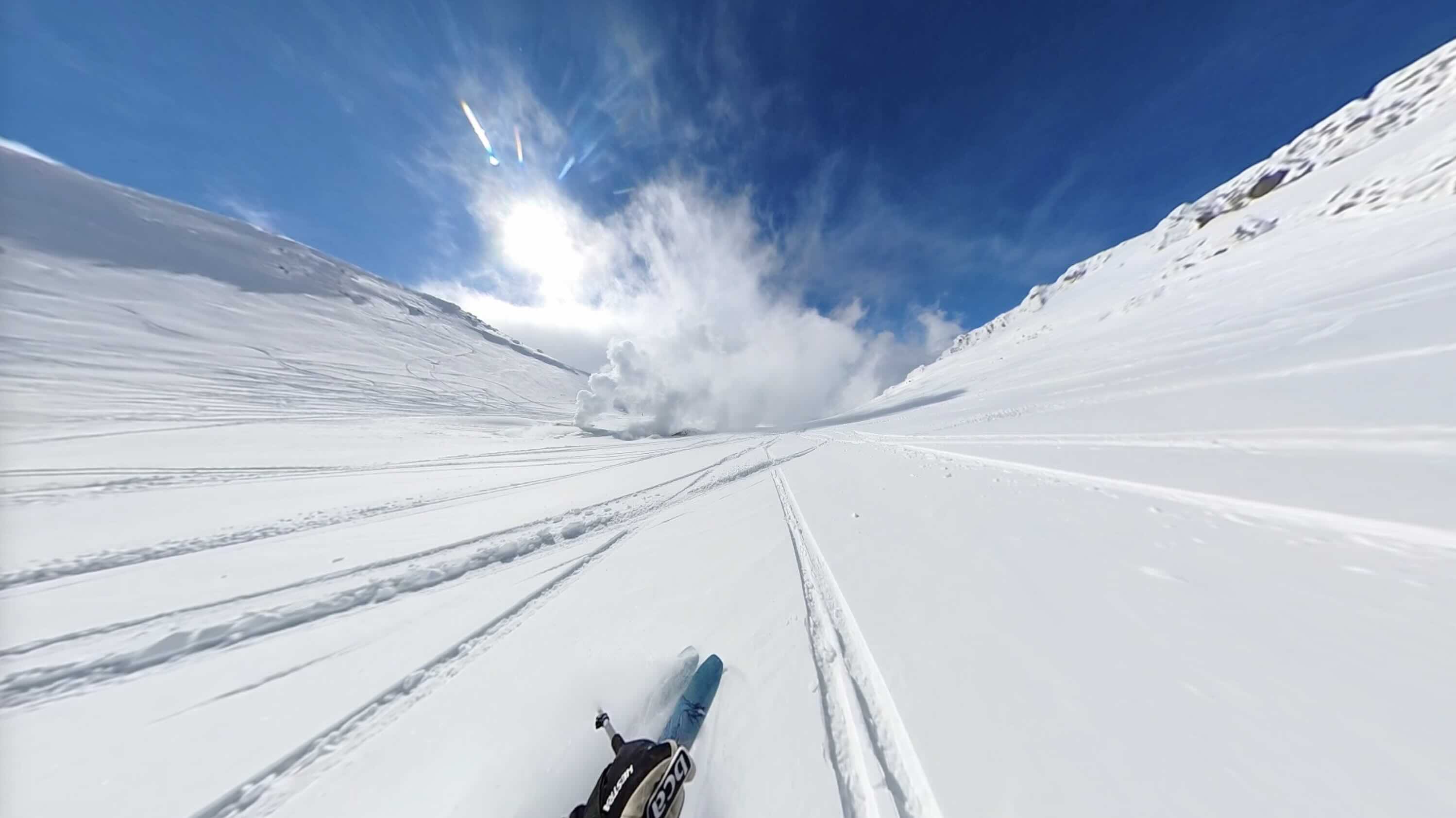 First-person view skiing down a wide open bowl on Asahidake, ski tips visible at the bottom of the frame, volcanic fumaroles steaming directly ahead against a bluebird sky.